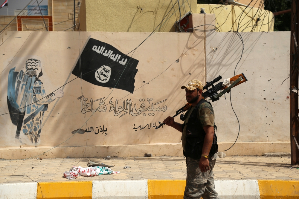 伊拉克部隊走過一面畫有伊斯蘭國常用旗幟的牆。（湯森路透）
