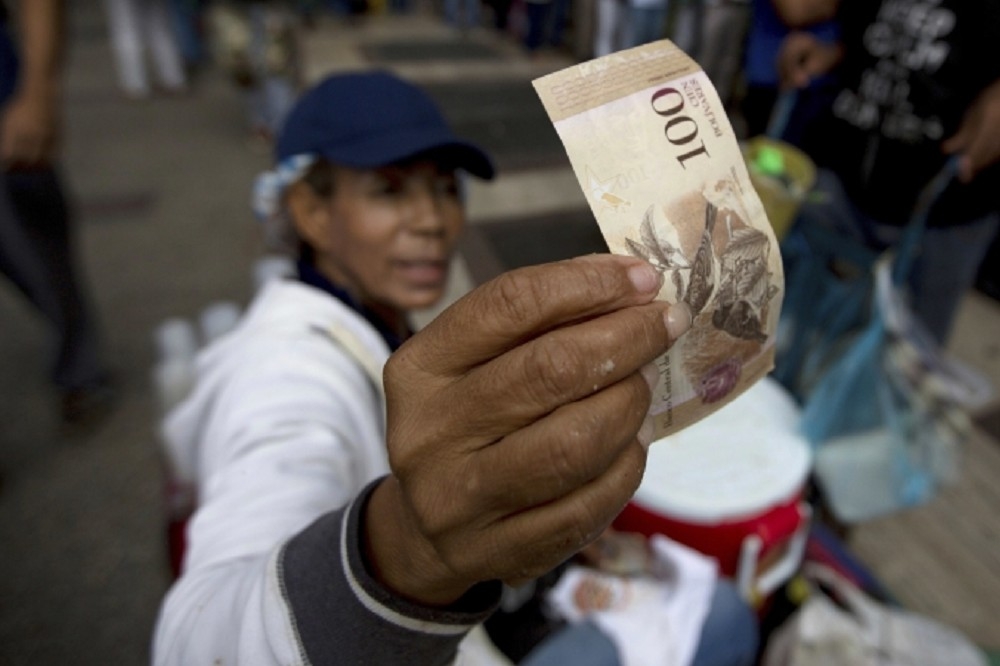 民眾拿著即將遭到廢棄的100玻利瓦紙鈔。（美聯社）