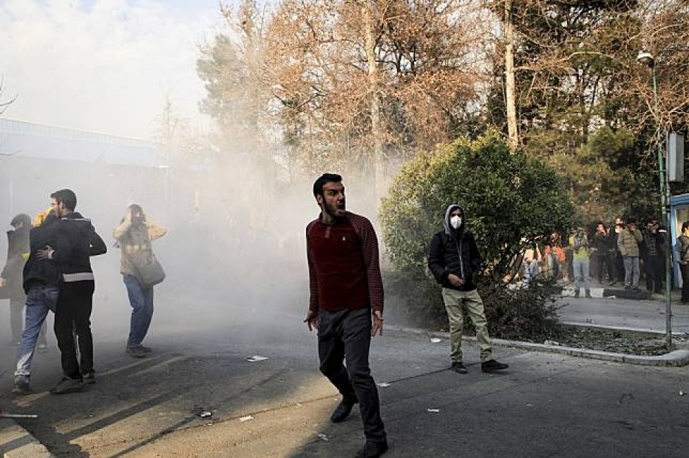 伊朗的示威民眾，一旁是鎮暴警察釋放的催淚瓦斯的煙霧。（美聯社）