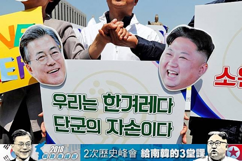 兩韓峰會27日舉行，人們戴著文在寅及金正恩面具象徵性的握手。（照片：湯森路透，後製：李明維）