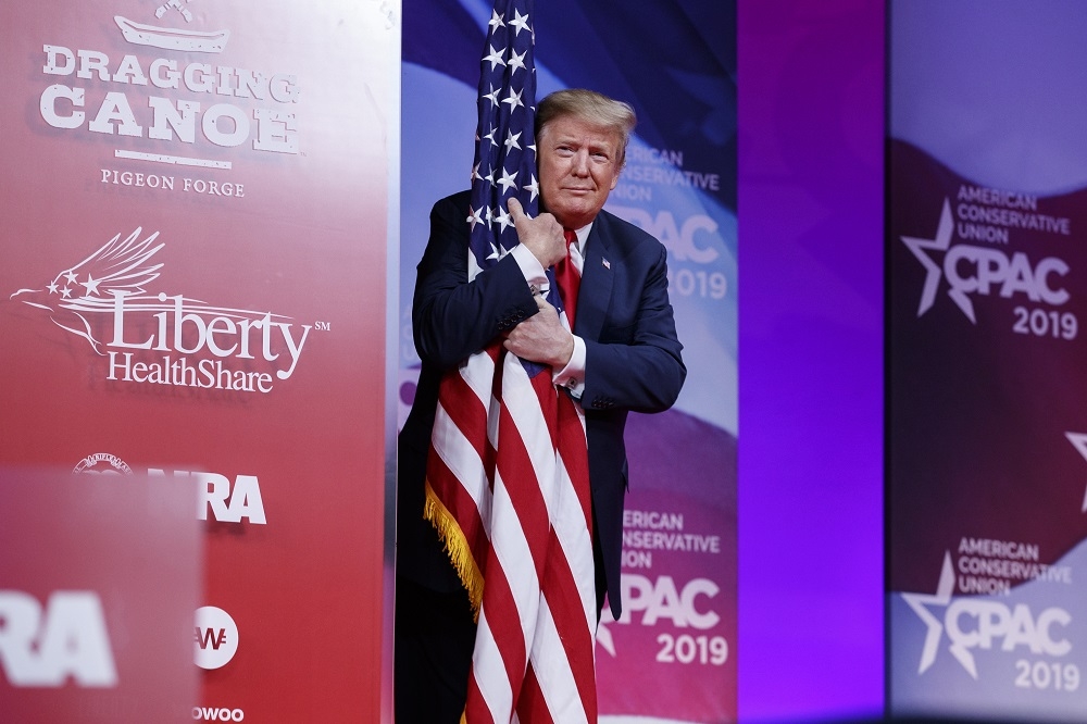 美國總統川普在會議期間擁抱美國國旗。（美聯社）