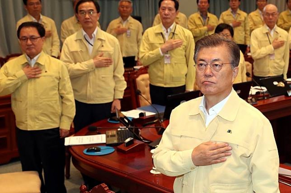 南韓總統文在寅（前）21日在內閣會議上向國旗致意。（湯森路透）