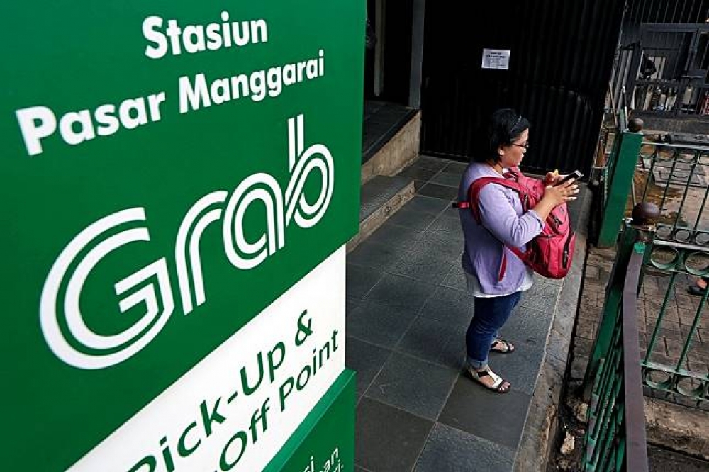 在印尼的火車站外，一名婦女在Grab的接送站旁使用手機。（湯森路透）
