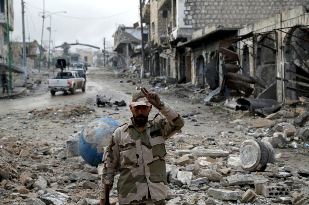 一名敘利亞士兵在殘破不堪的城鎮街道前拍照。（湯森路透）