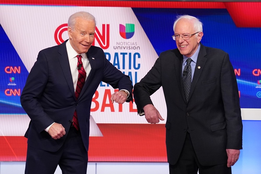武漢肺炎疫情升溫，拜登（左）和桑德斯15日出席民主黨初選辯論會時，用碰手肘取代握手。（湯森路透）