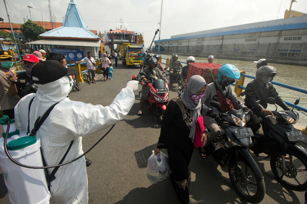印尼防疫人員對街頭來往車輛和行人進行消毒。（湯森路透）