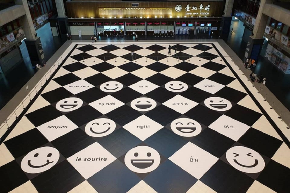 台鐵決定不明文禁坐，並在原先黑白棋格盤的大廳換上「笑臉」字樣的新地貼，以及寫著「微笑」的10種語文，展現友善包容的新風貌。（取自台鐵管理局臉書）