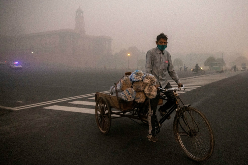 戴口罩上街的新德里三輪車小販與身後驚人的霧霾。（湯森路透）