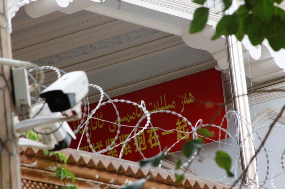 2018年9月6日，中國新疆維吾爾自治區一座清真寺的牆壁上放著一面宣傳橫幅和一台監視器。（湯森路透）