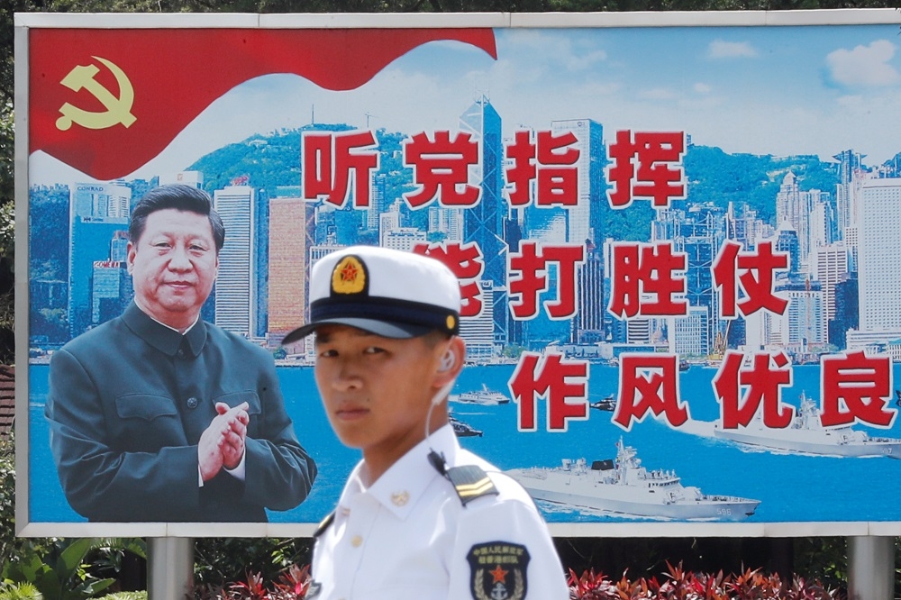 一名人民解放軍海軍站在香港一座習近平的宣傳標語前。（湯森路透）