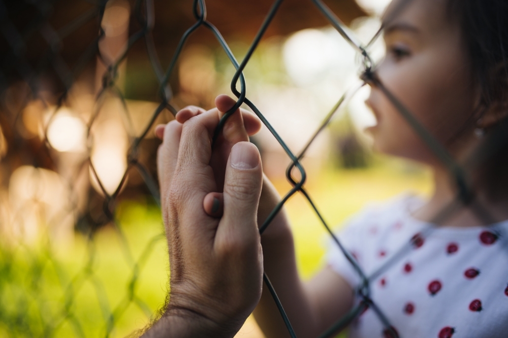 （2021 © Nenad Stojkovic , A loving scene of a parent and a child holding hands through a wire fence. @ Flickr, CC BY-SA 2.0.）