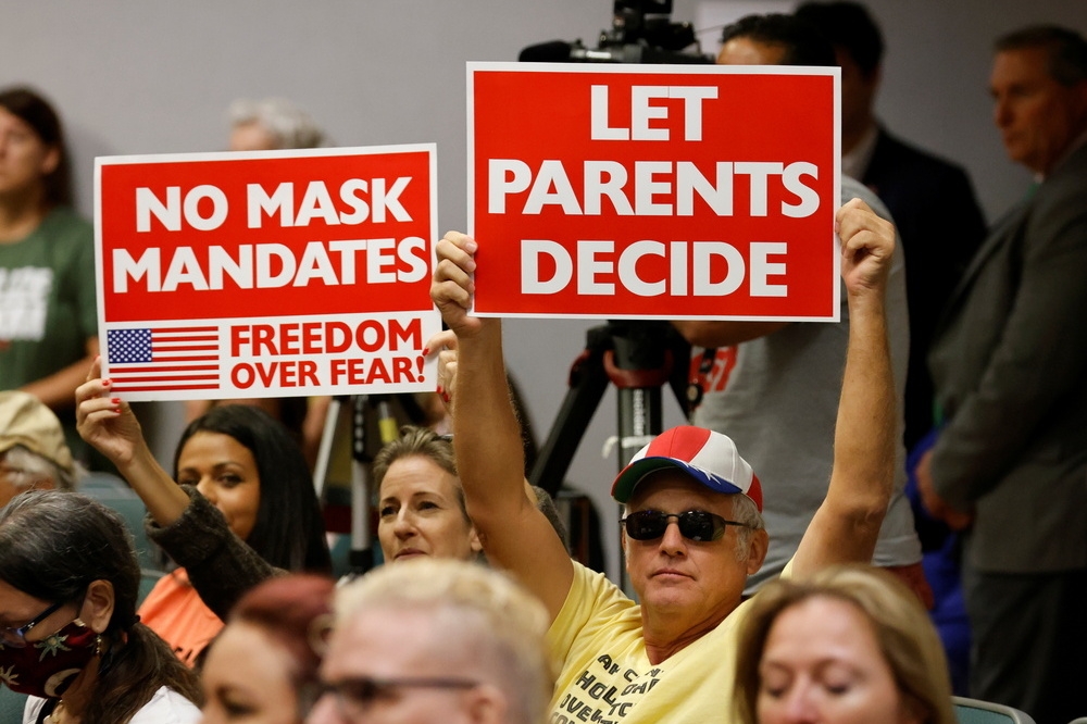 佛州學校召開公聽會，反對強制戴口罩的家長高舉海報，要求校方讓「家長自由決定」。（湯森路透）