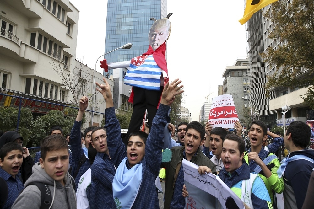 伊朗首都德黑蘭街頭，學生手持諷諭川普的頭像，抗議美國退出伊朗核協議的主張。（美聯社）