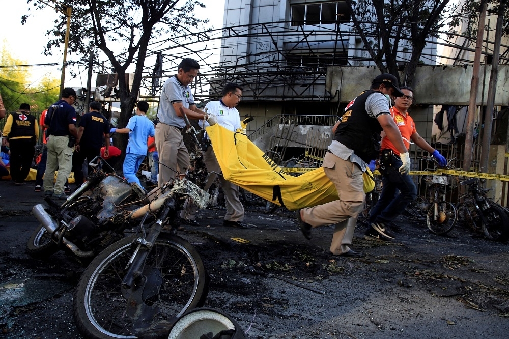 救難人員移動燒焦的摩托車旁的罹難者遺體。（湯森路透）