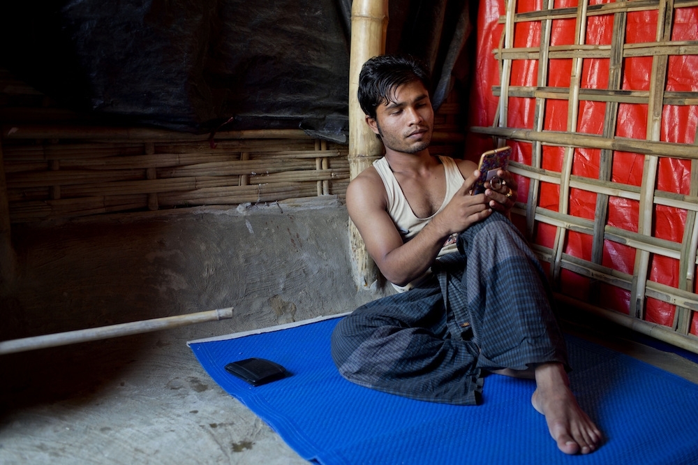 22歲的烏拉坐在由塑膠板料以及竹子建造而成的屋子裡，用手機翻看以往拍下的影片。（美聯社）