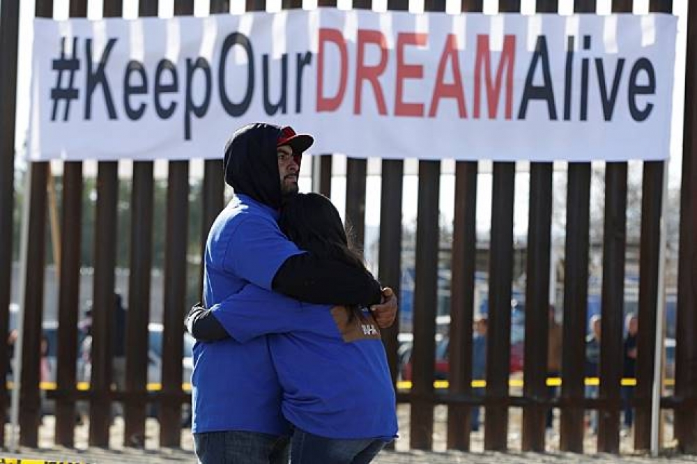 移民在美墨邊界高牆前擁抱。（湯森路透）