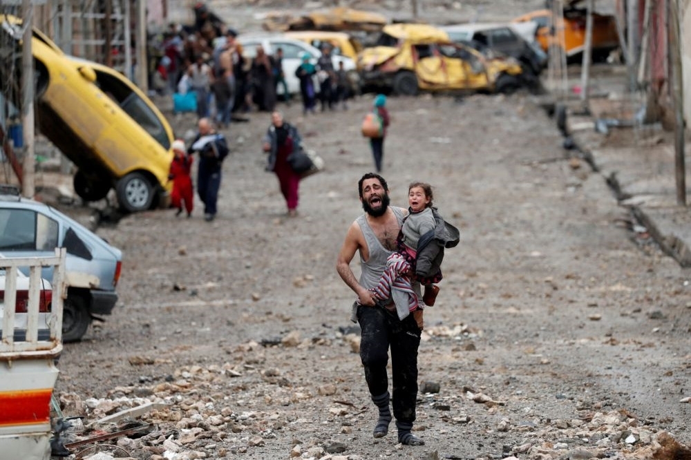 在受到「伊斯蘭國」（IS）控制的伊拉克大城摩蘇爾（Mosul），一名男子抱著小孩走向伊拉克軍隊。（湯森路透）