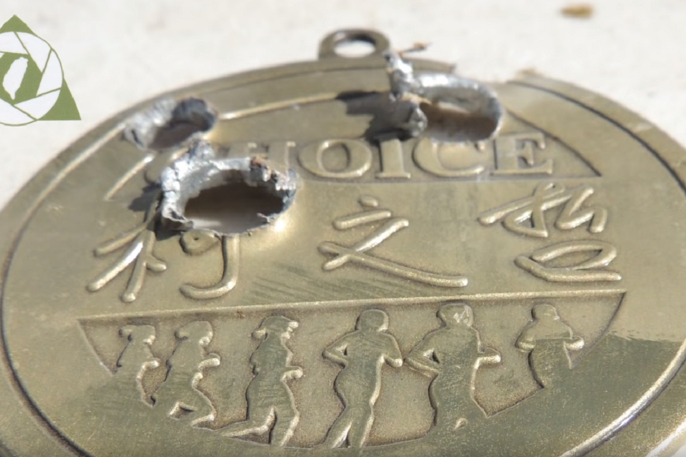影片展示柯文哲假金牌被子彈貫穿3孔的畫面，怵目驚心。（圖片取自LATWTVTaiwanYouTube）