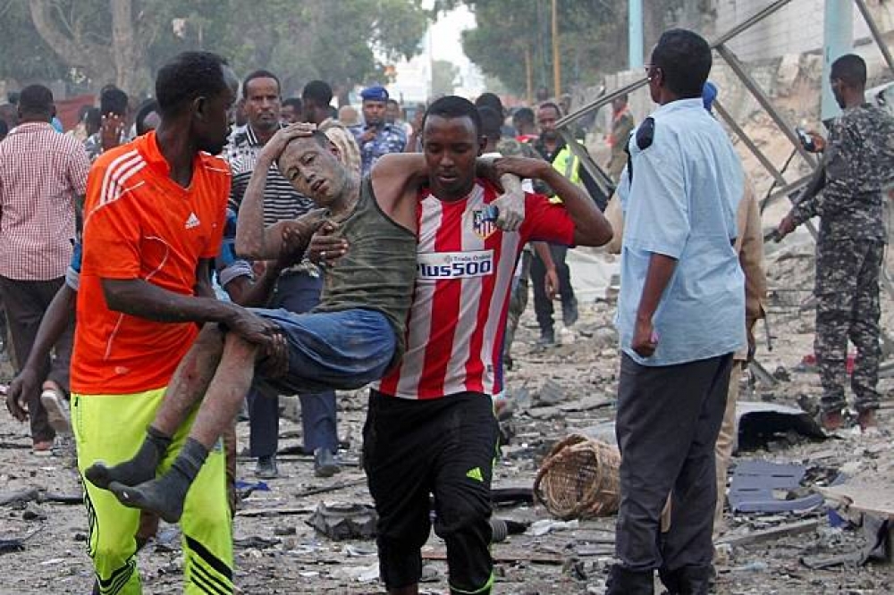 索馬利亞民眾從案發現場抬出傷者。（湯森路透）