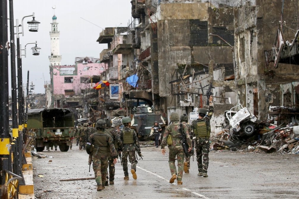 菲律賓軍隊走過馬拉威市一條街道，周圍斷垣殘壁，等待整理。（美聯社）