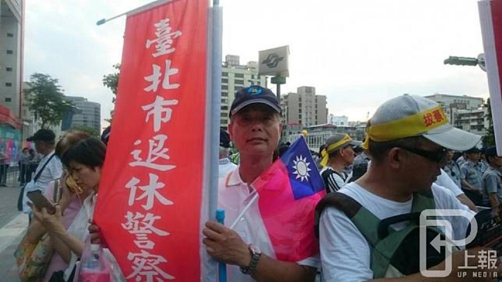 現場反年改抗議民眾持標語與國旗、一方面抗議年金改革、同時也替台灣隊加油。（攝影：羅佳蓉）。
