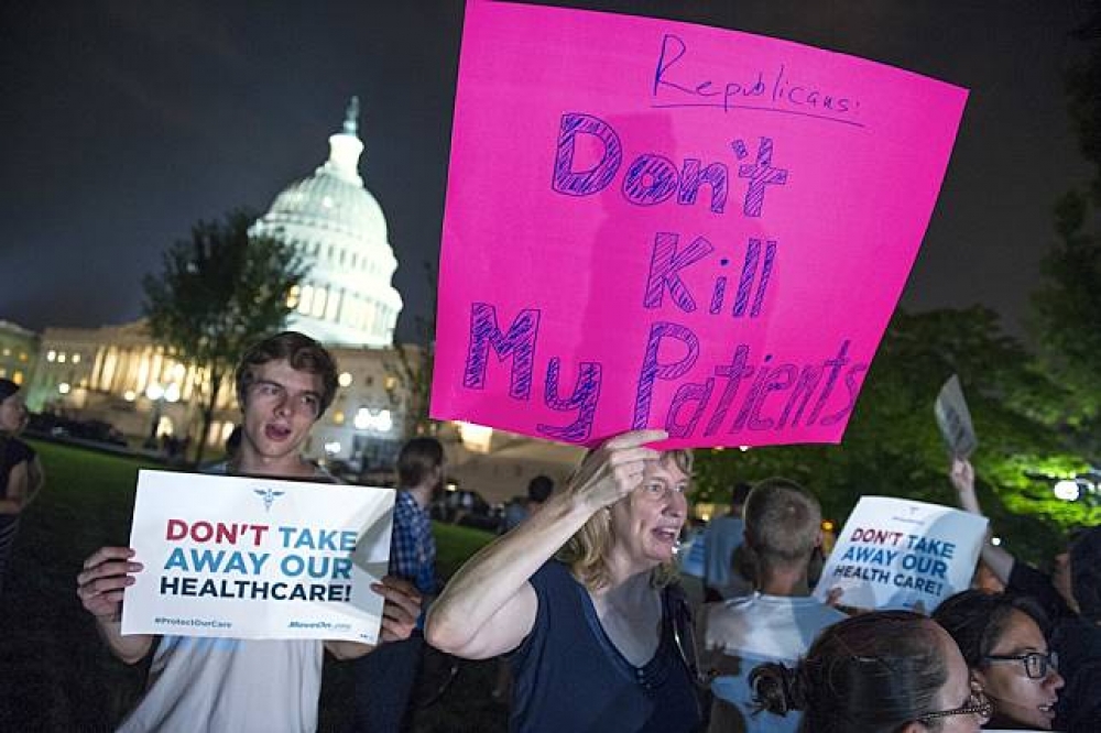 美國民眾27日在國會外抗議共和黨欲廢除「歐巴馬健保」的打算。（美聯社）