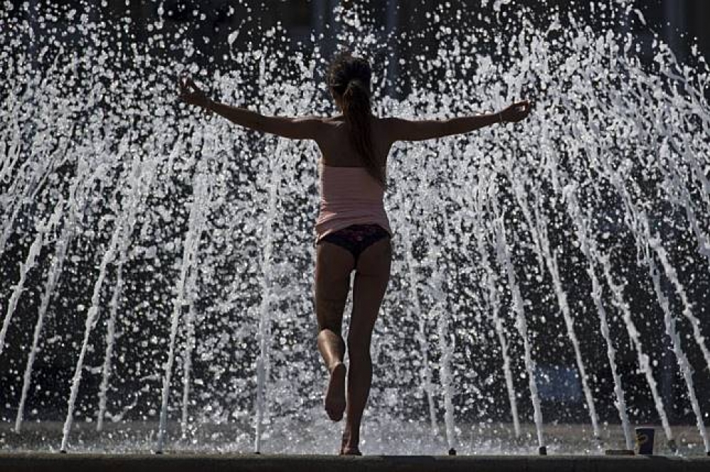 因為酷暑，民眾在噴泉上練習瑜珈消暑。（美聯社）
