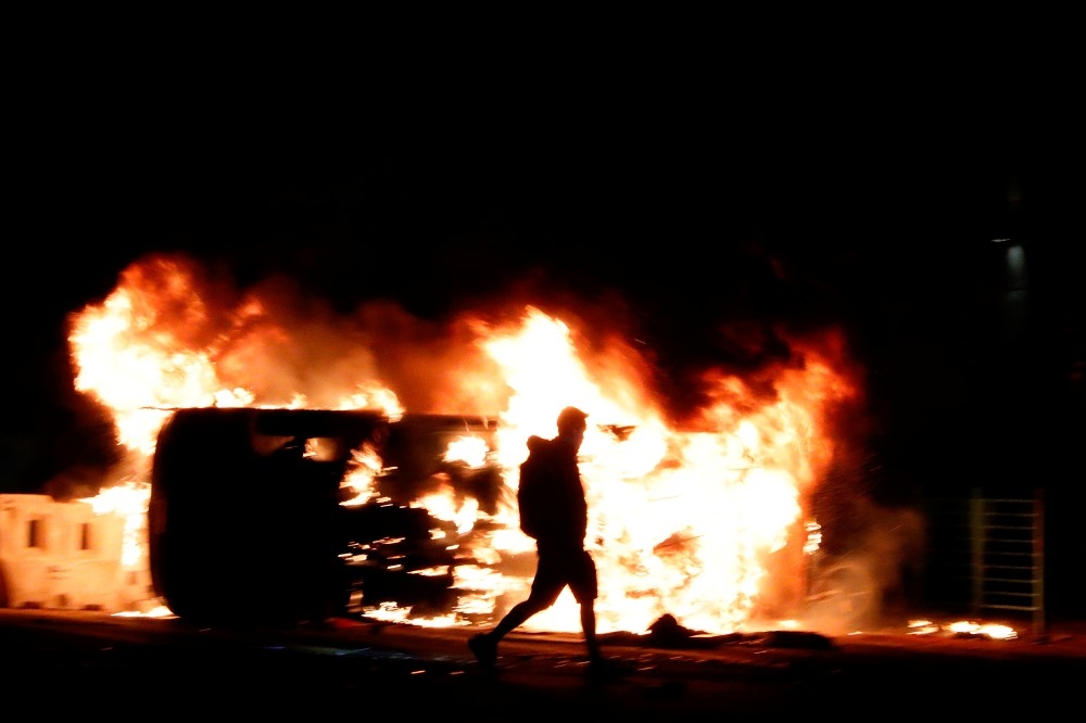 香港示威者11日晚間走過將軍澳一輛焚燒中的車輛。（湯森路透）