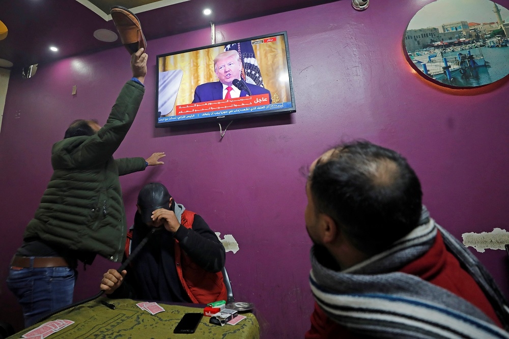 西岸的巴勒斯坦民眾28日作勢鞋攻電視裡的川普。（湯森路透）