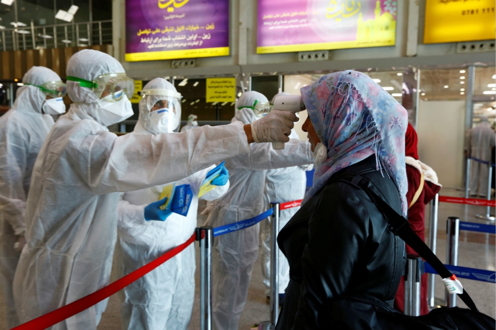 伊拉克機場人員穿著全套防護衣，對著外來旅客測量額溫。（湯森路透）