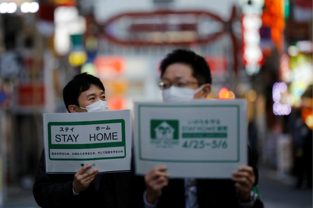 日本防疫人員高舉海報，提醒民眾減少出門。（湯森路透）