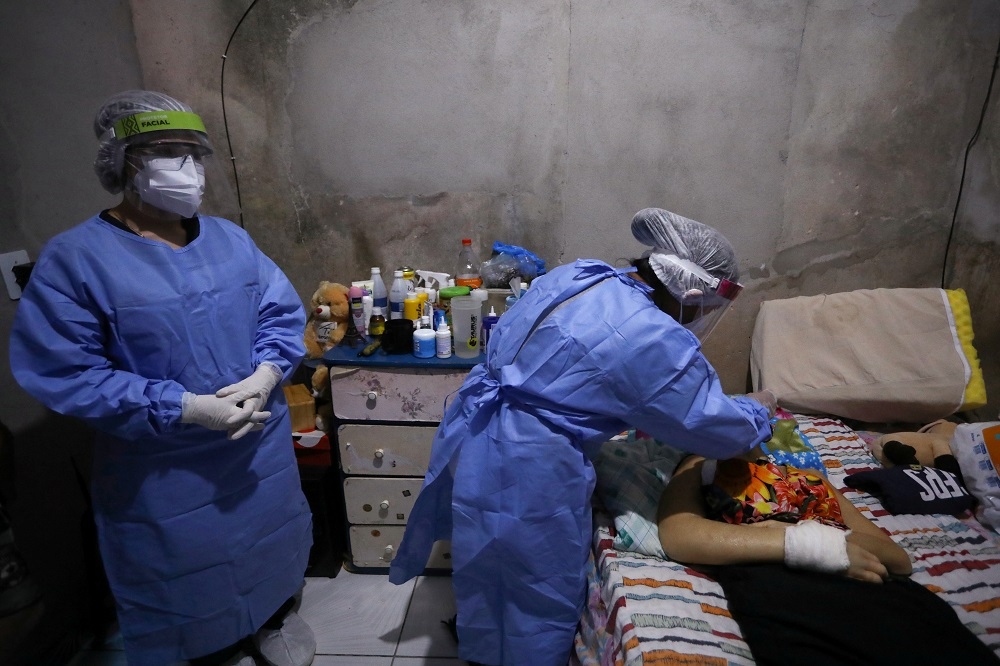 巴西一名57歲的婦女死於新冠肺炎，圖中醫護人員前往死者家中採集檢體樣本。（湯森路透）