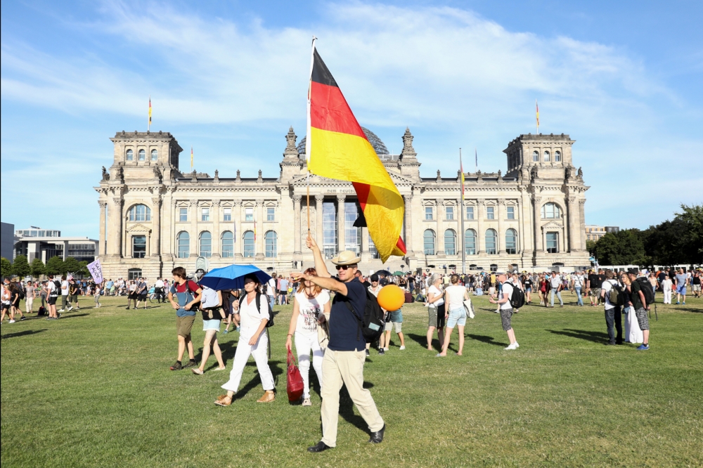 德國柏林1日在抗議政府對新冠病毒施加限制的示威遊行中，一名示威者高舉德國國旗。（湯森路透）