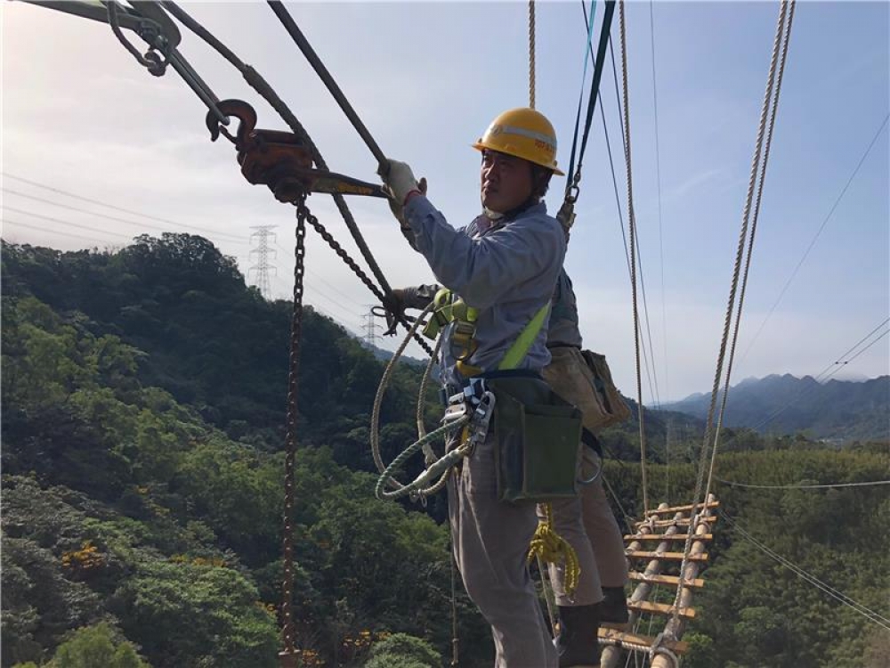 台電員工身著防護設備，在數十公尺高的空中進行緊線作業工程。（台電提供）