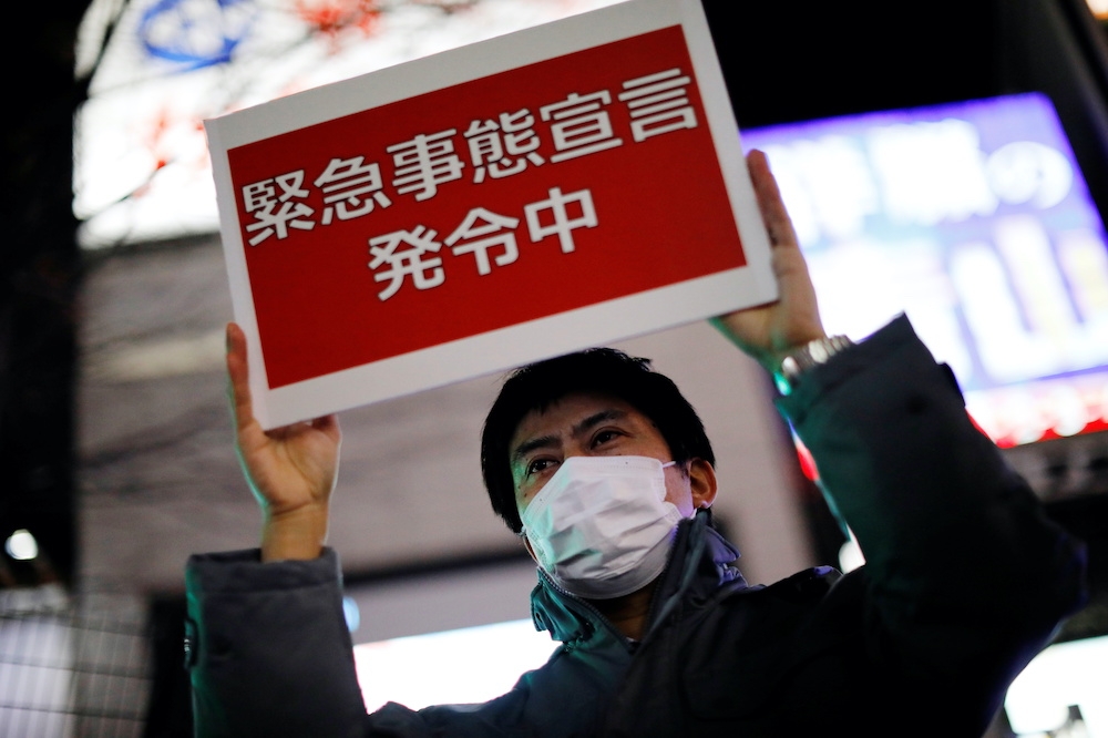 東京都廳工作人員高舉「緊急事態宣言」標語牌，呼籲民眾待在家中。（湯森路透）