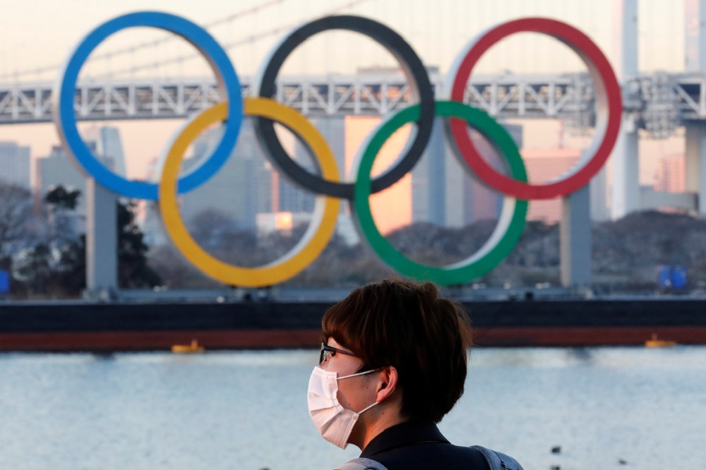 一名戴著口罩的男子站在東京奧運五環標誌前。（湯森路透）