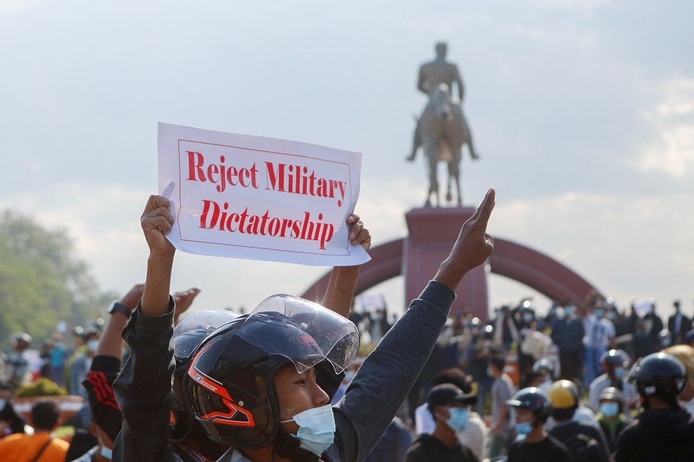 2 月 8 日緬甸抗議行動，示威者一手高舉標語，一手比出象徵反獨裁的三指。（湯森路透）