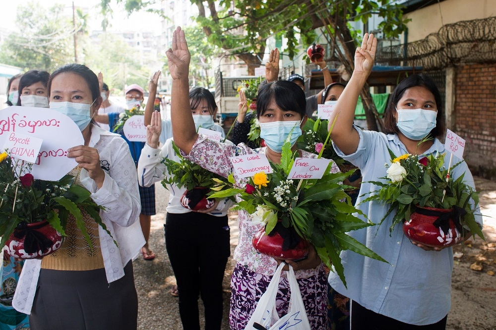 緬甸仰光民眾在新年期間一手捧鮮花、一手高舉三指訴求民主，今年並無歡慶佳節的氣氛。（湯森路透）