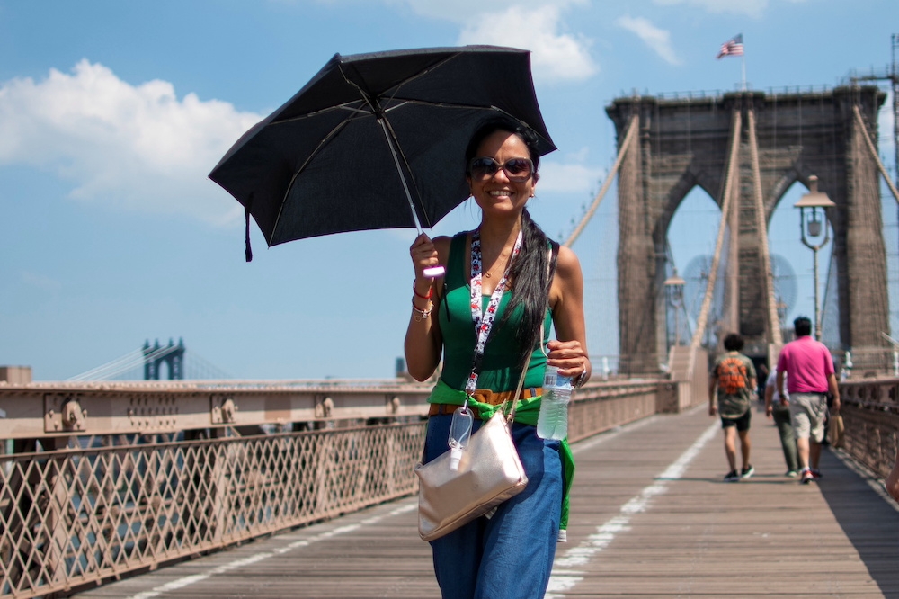6月熱浪席捲全美下，一名女子在行走在紐約布魯克林大橋上陽傘得撐好撐滿。（湯森路透）