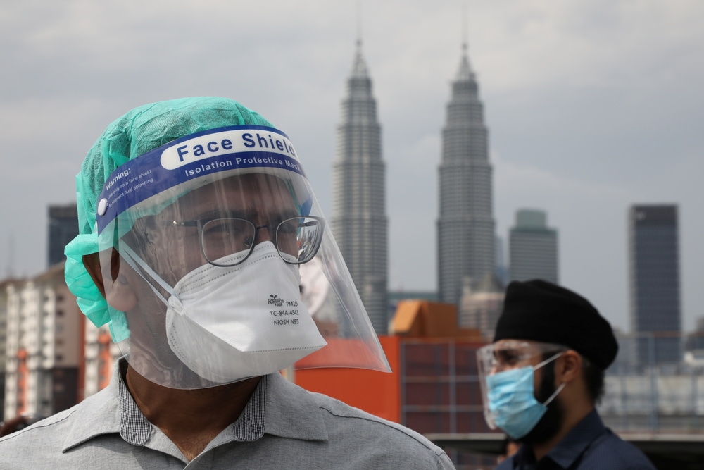 馬來西亞防疫人員在街頭提醒民眾保持社交距離。（湯森路透）