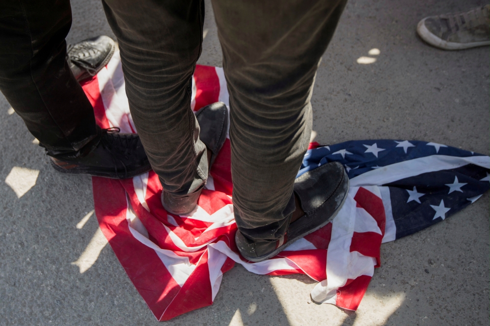 不滿美國遣返將海地難民遣返，大批民眾在美國大使館外抗議、踩踏美國國旗。（湯森路透）