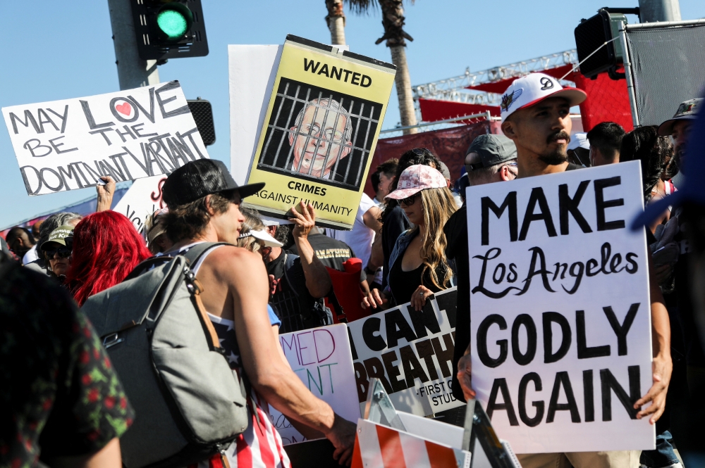 美國西部大城洛杉磯的反疫苗抗議群眾，右下角的牌子寫著「讓洛城再次『神聖』」。（湯森路透）