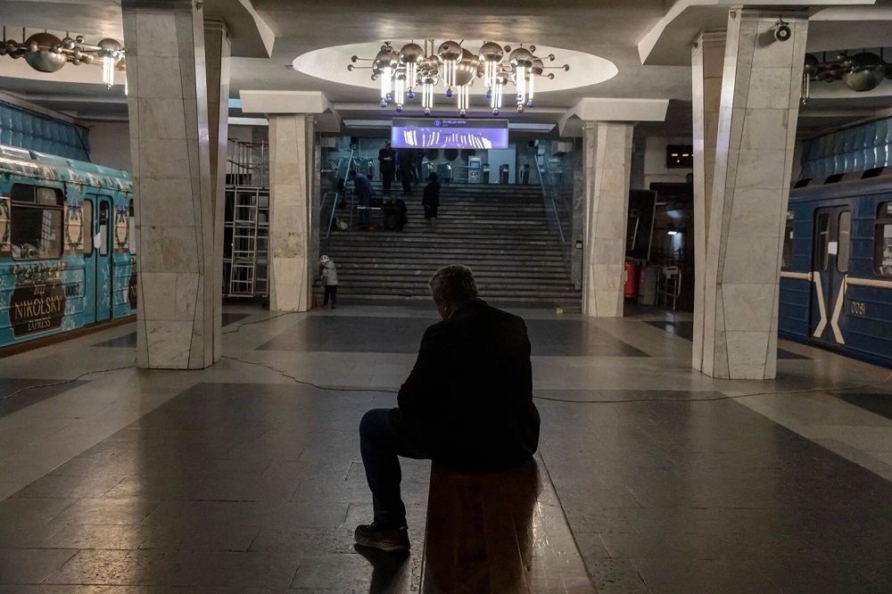 一個男人坐在地鐵的長椅上，兩旁的車廂現在住著人，人們在地鐵站躲避持續不斷的轟炸。烏克蘭，2022 © Adrienne Surprenant/MYOP