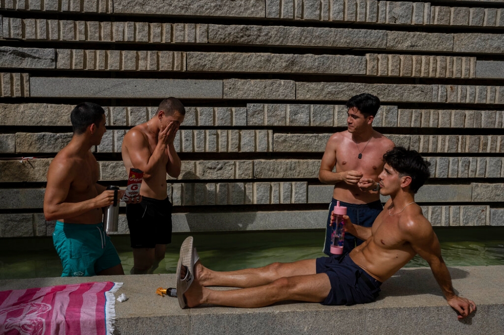 西班牙遭遇熱浪來襲，民眾在噴泉旁消暑納涼。（美聯社）