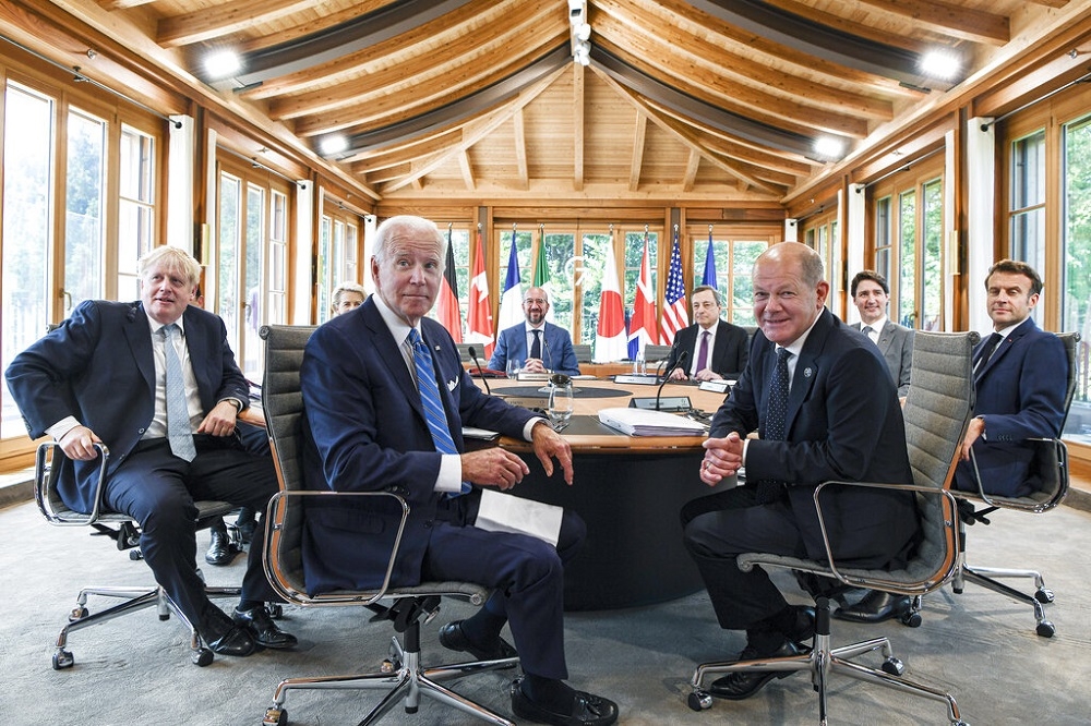 G7領袖坐在會議桌前準備共進午餐，過程中英國首相強生（前左一）開起俄國總統普丁的玩笑。（美聯社）