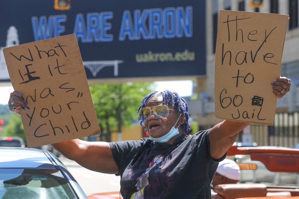 一名非裔女性一手舉著「如果是你的孩子呢」，另一手舉著「他們該去坐牢」的標語，替遭警方擊斃的沃克討公道。（美聯社）