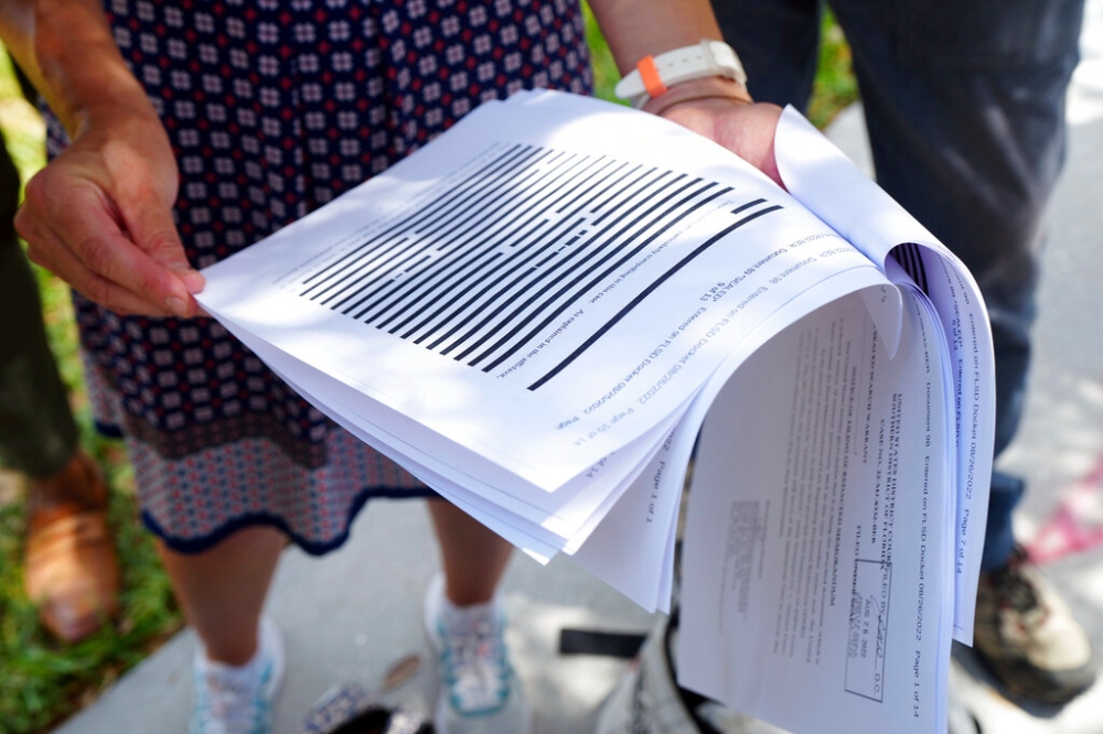 記者們26日聚集佛州地方法院外閱讀司法部公開的FBI宣誓書，內容詳述聯邦探員何以搜索川普的海湖莊園。（美聯社）