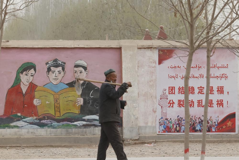 新疆农民走在喀什市街道上，身后是中国的政治宣传标语。（美联社）(photo:UpMedia)