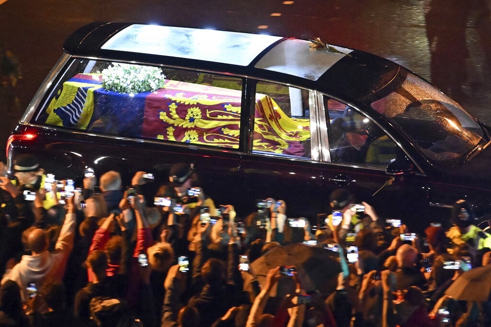 女王靈車抵達倫敦，民眾在路邊舉起手機捕捉這一刻。（美聯社）