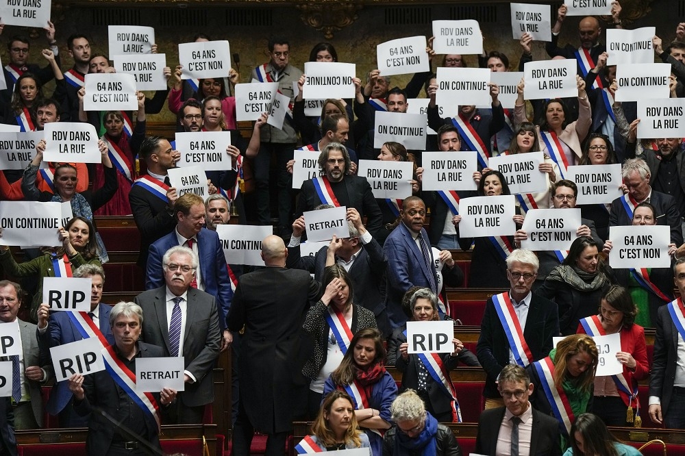 法國國民議會左派議員20日在不信任案投票未通過後，展示標語抗議。（美聯社）